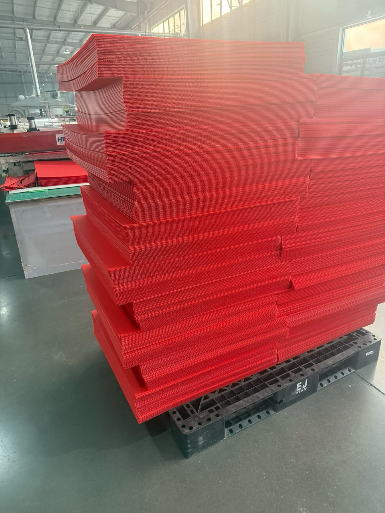 Red PP hollow sheets stacked on pallet before conversion into custom boxes