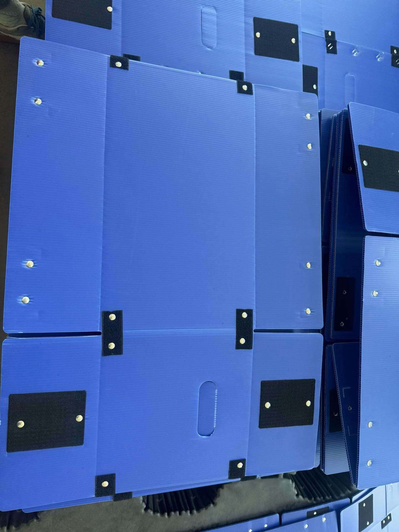 Flat-packed blue PP corrugated box panels with closures and riveted details